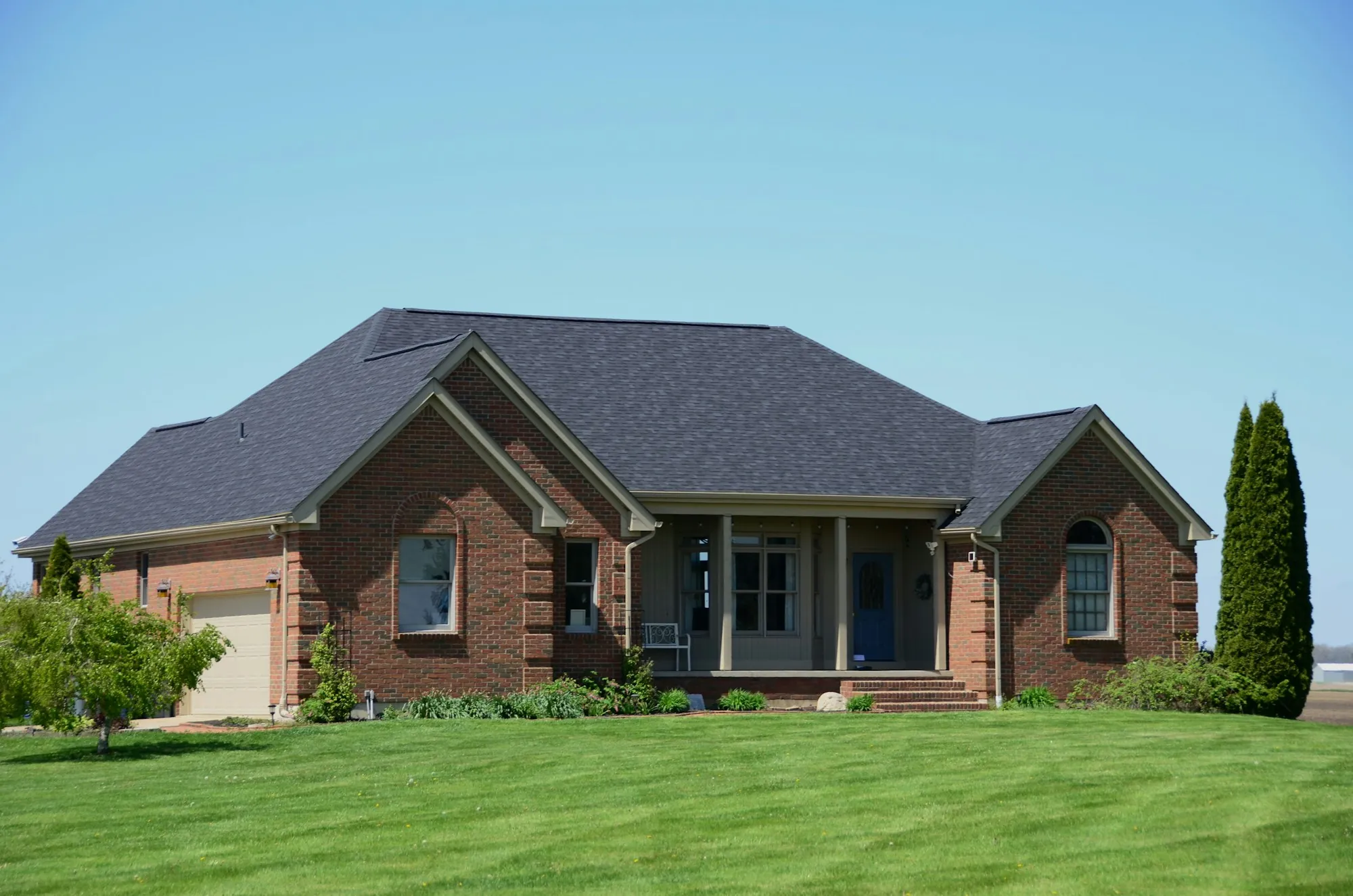 Brick ranch house with a hip roof and tall cypress trees